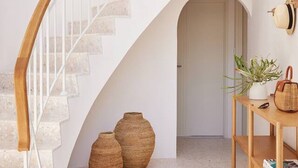 A white staircase with wooden handrails, leading to an upper level. There are two large woven baskets on the floor and a wooden shelf with a plant and a hat. - Amazing 3bd in National Park (Bundeena)