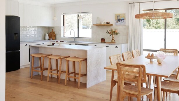 A modern kitchen with white cabinetry, a central island with bar stools, a dining table with chairs, and pendant lighting. - Amazing 3bd in National Park (Bundeena)