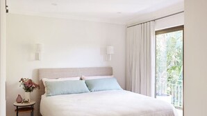 A bedroom with a bed, bedside lamps, a nightstand with a vase, and a window with curtains. - Amazing 3bd in National Park (Bundeena)