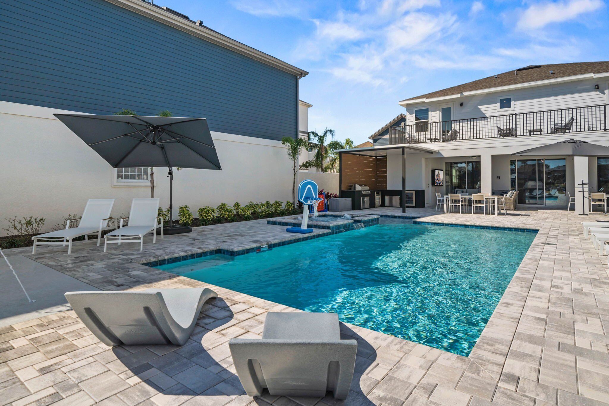 A swimming pool with lounge chairs and an umbrella, surrounded by a patio area with a brick floor.