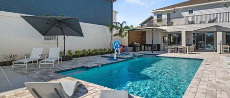 A swimming pool with lounge chairs and an umbrella, surrounded by a patio area with a brick floor.