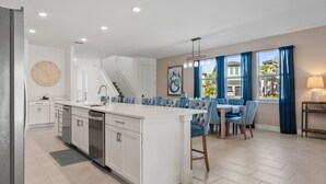 Une cuisine moderne avec des meubles blancs, un îlot central et un coin repas doté de chaises recouvertes d’un tissu bleu.