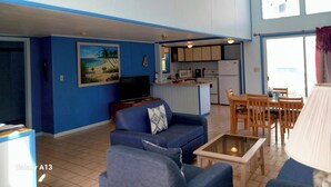A spacious living area with a blue sofa, a coffee table, and a TV. A kitchen is visible in the background with a microwave and stove. - Charming Standalone 3-bedroom villa with AC and WiFi in lovely Frigate Bay (Frigate Bay)