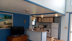 A compact kitchen with a microwave, stove, and refrigerator. A wooden TV stand and a dining table with chairs are in the living area. - Charming Standalone 3-bedroom villa with AC and WiFi in lovely Frigate Bay (Frigate Bay)