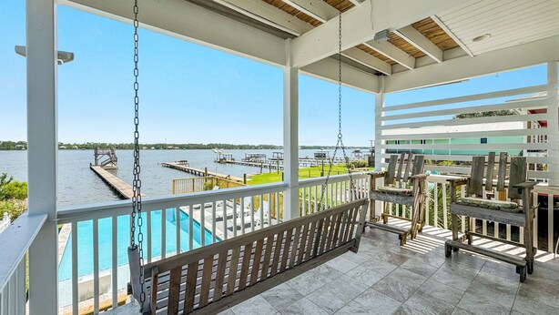 A covered outdoor area with a swing, a pool, and a view of the water and dock.