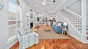 A spacious living room with a fireplace, a blue sofa, and a staircase with white railings.