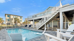 Une piscine avec un toboggan, des chaises longues et un escalier menant à une terrasse supérieure.