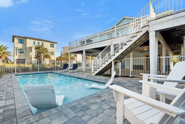A swimming pool with a slide, lounge chairs, and a staircase leading to an upper deck.
