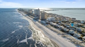 An aerial view of a coastal area with a beach, beachfront properties, and a pier extending into the water.