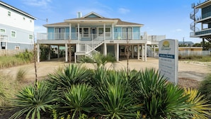 Une propriété située en bord de mer, comprenant une grande maison, une piscine privée et un panneau publicitaire pour la location de logements de vacances.