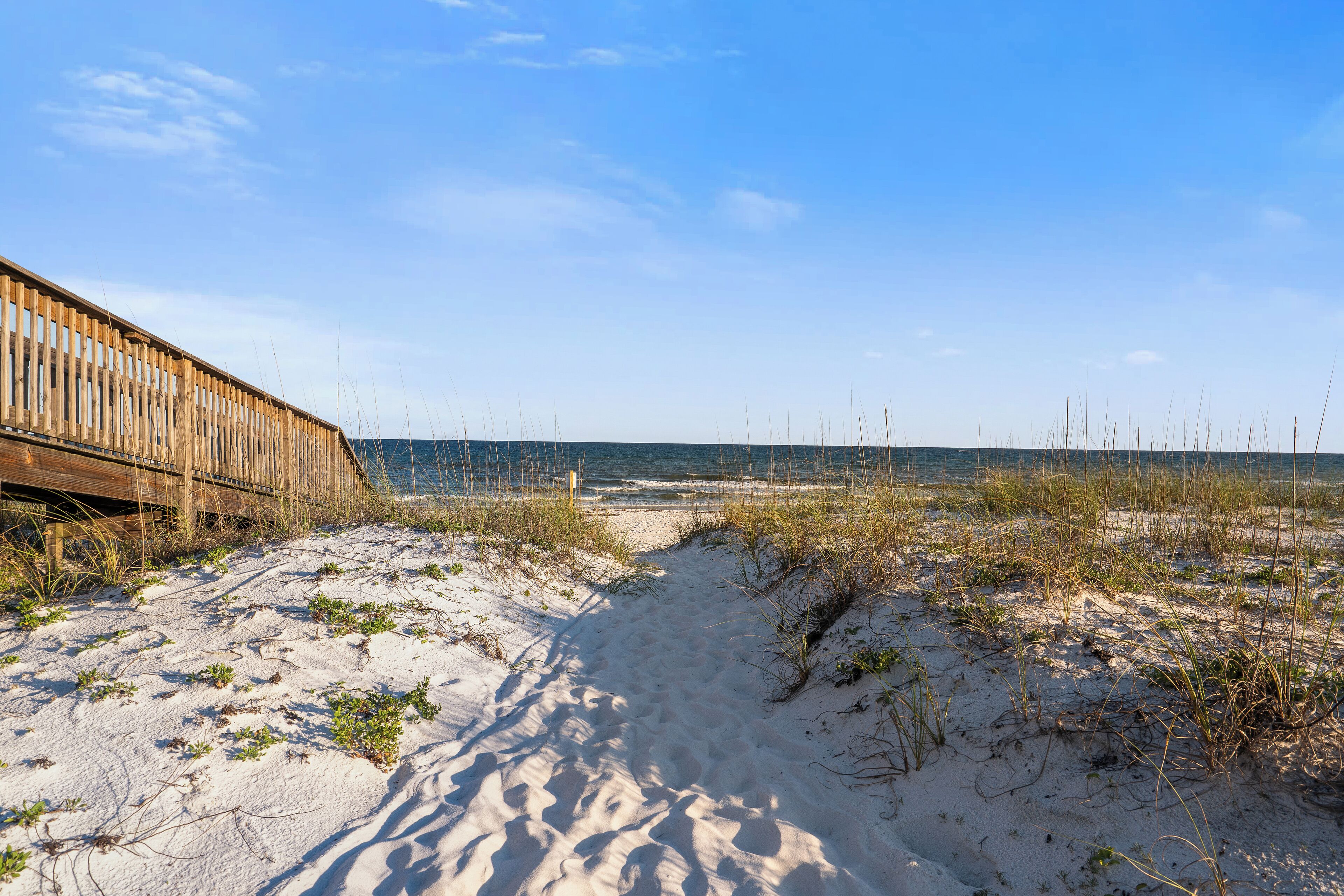 A sandy beach path leading to the ocean with a wooden boardwalk on the left.