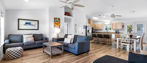 Amplia sala de estar con sofá, reposapiés y mesa de centro, una cocina con armarios de madera y un comedor con sillas y mesa.