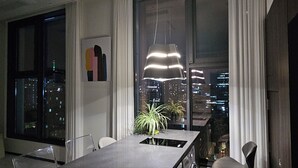 Een moderne eetruimte met uitzicht over de stad, een tafel met stoelen en een hanglamp.