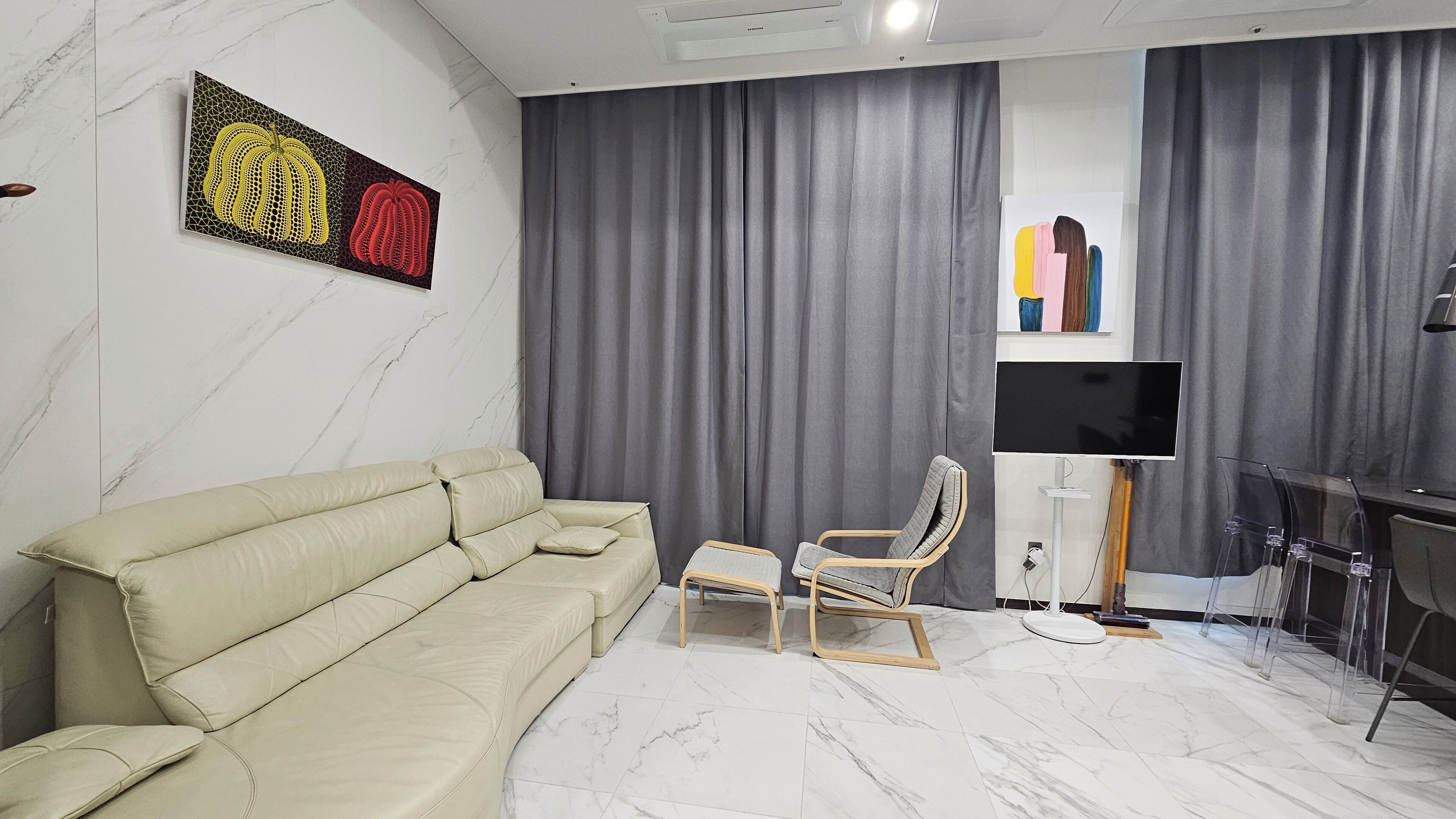 A modern living room with a beige sofa, a wooden chair, a flat-screen TV, and grey curtains.