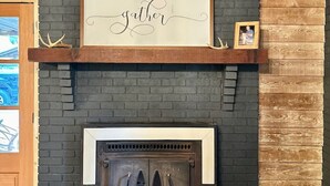 Una chimenea con un cartel que dice 'Gather', una repisa de madera y una pared de ladrillo.