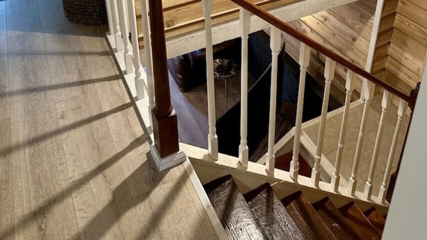 Una escalera de madera con balaustres blancos y un candelabro colgante.