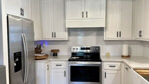 Una cocina con armarios blancos, un refrigerador de acero inoxidable, un horno y un ventilador de techo.