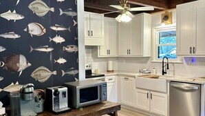 Una cocina con armarios blancos, techo de madera y papel tapiz con motivos marinos.