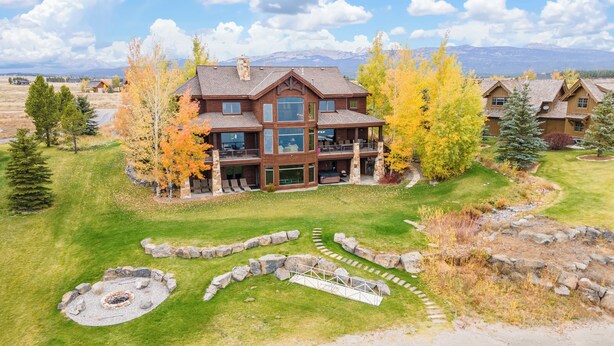 A large, multi-story wooden house with a stone fireplace, surrounded by a well-maintained lawn and autumn trees. - Large Home | Reservoir Views & Access | Hot Tub | Fire Pit | Basketball Court (Island Park)