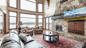 A spacious living room with large windows, a fireplace, and a view of the outdoors. - Large Home | Reservoir Views & Access | Hot Tub | Fire Pit | Basketball Court (Island Park)