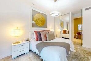A modern bedroom with a large bed, bedside lamps, a mirror, and a decorative wall piece. - Indian Wells Chic Villa with fire pit, patio, kitchen, pool, and majestic views (Indian Wells)