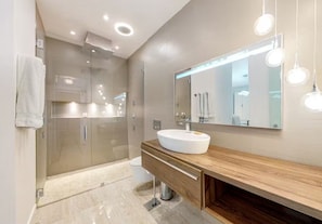 A modern bathroom with a glass shower enclosure, a wooden vanity with a white sink, and a large mirror with integrated lighting. - Indian Wells Chic Villa with fire pit, patio, kitchen, pool, and majestic views (Indian Wells)