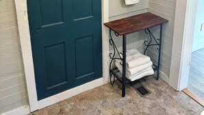 A bathroom with a teal door, a small wooden table with towels, and a towel rack.