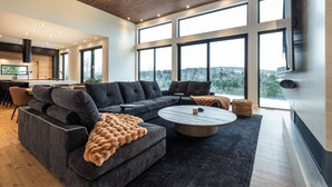 A modern living room with a sectional sofa, a round coffee table, and large windows offering a view of the outdoors.