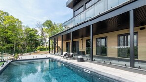 A modern outdoor pool area with a glass-enclosed patio, outdoor seating, and a staircase leading to an upper level.