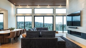A modern living room with a large sectional sofa, a dining table with chairs, and a flat-screen TV mounted on the wall.