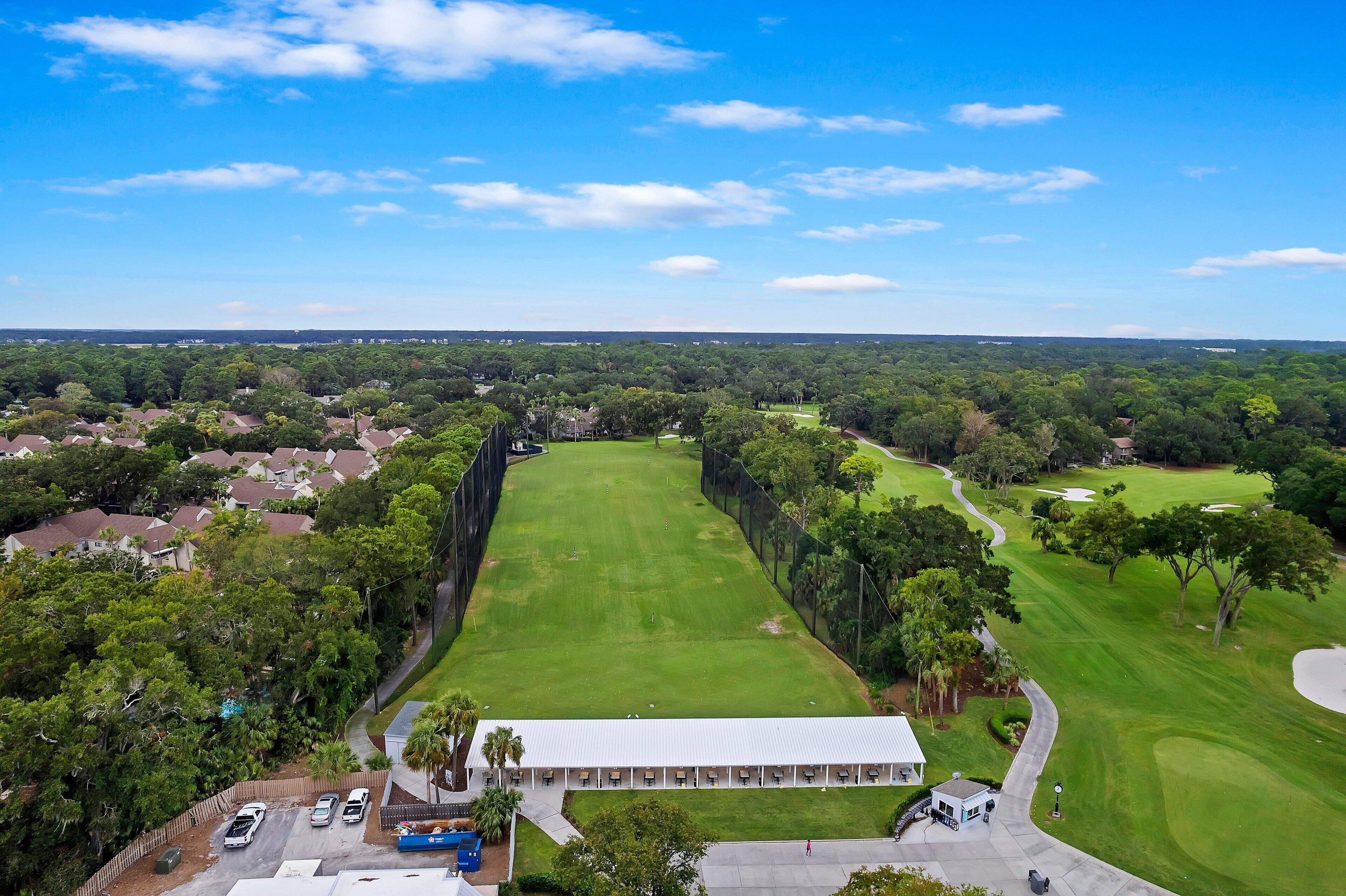 Une vue aérienne d’un terrain de golf avec un club-house, entouré de zones résidentielles et d’une végétation luxuriante.