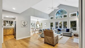 A spacious living area with a high ceiling, a dining area, and large windows.