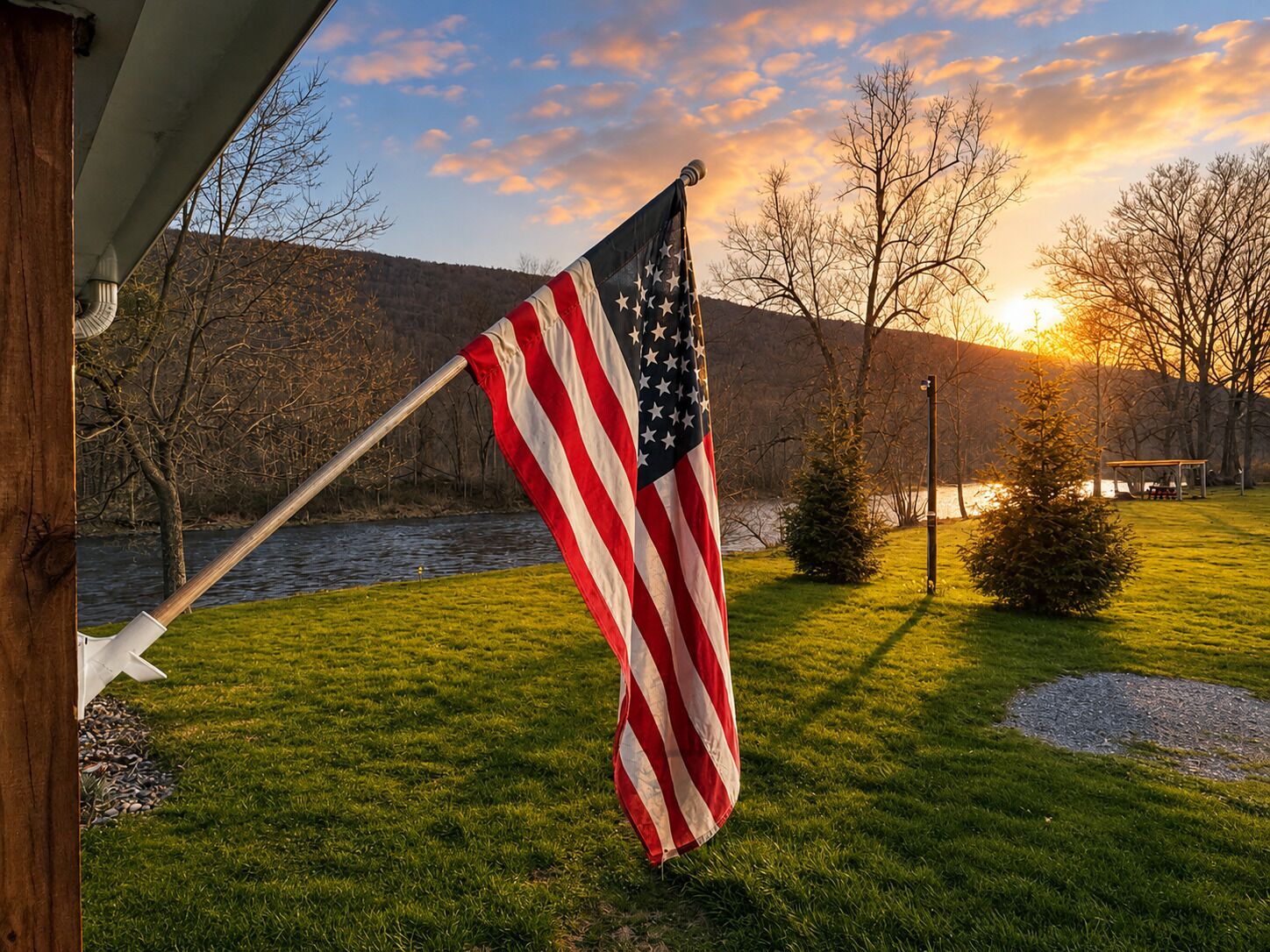 An American flag on a flagpole in a grassy area with a body of water and trees in the background.