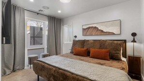 Une chambre à coucher moderne avec un grand lit, une fenêtre avec des rideaux, un tableau au mur et une lampe de chevet.