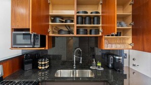 Une cuisine avec des meubles de rangement en bois, un évier en acier inoxydable, un four à micro-ondes et une machine à café.