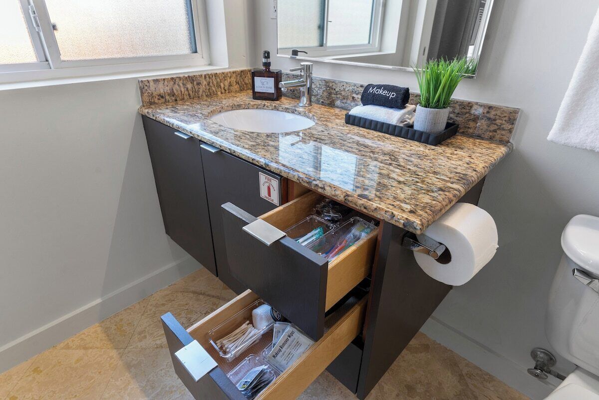 A bathroom with a granite countertop sink, a mirror above it, a makeup station, and a toilet.