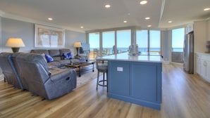 A spacious living room with a gray sofa, a coffee table, and a view of the ocean through large windows. - Stunning 2BR/2BA Oceanfront Penthouse at Maisons-Sur-Mer in Myrtle Beach (Myrtle Beach)