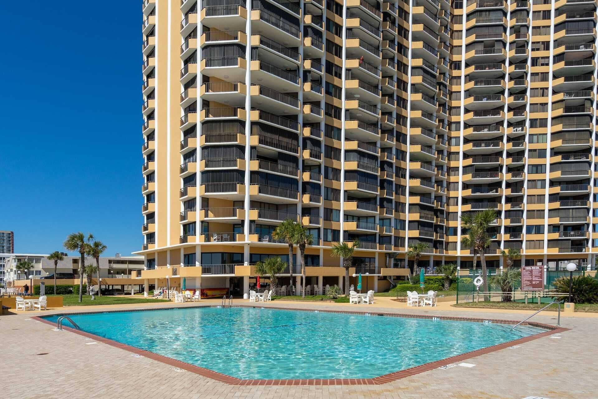 A high-rise hotel with multiple balconies, a swimming pool, and outdoor seating areas.