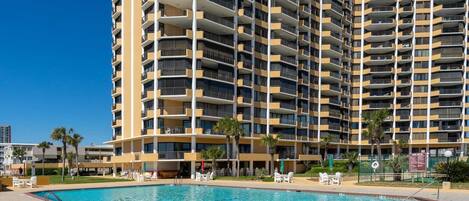 A high-rise hotel with multiple balconies, a swimming pool, and outdoor seating areas.