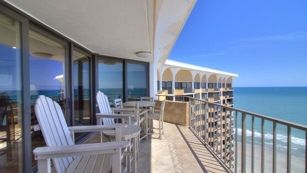 A balcony with white chairs and a table, overlooking the ocean. - Stunning 2BR/2BA Oceanfront Penthouse at Maisons-Sur-Mer in Myrtle Beach (Myrtle Beach)