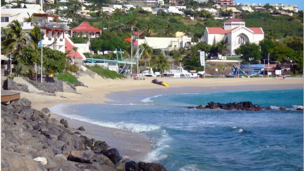 Uma cidade costeira com praia, falésias rochosas e edifícios com telhados vermelhos.