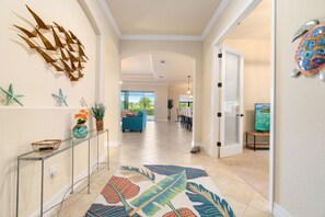 A hallway with a clear view to the living area, featuring a glass console table, decorative starfish, a patterned rug, and a turtle wall art piece. - Gorgeous, Modern 3-Bedroom Home Pool Home w/ Resort Amenities in Bonita National (Bonita Springs)