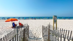 A beach with blue umbrellas and a wooden fence.