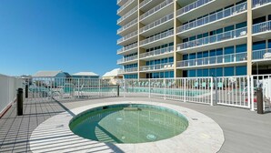 Un espace piscine avec un jacuzzi, entouré d’une clôture blanche, et un immeuble à plusieurs étages avec des balcons en arrière-plan.