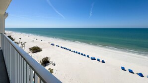 A beach view from a balcony with rows of blue beach chairs and a clear sky.