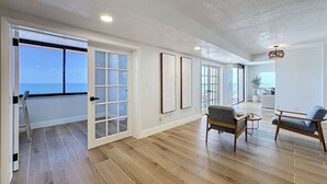 A spacious living area with wooden flooring, a balcony door, and a view of the sky.