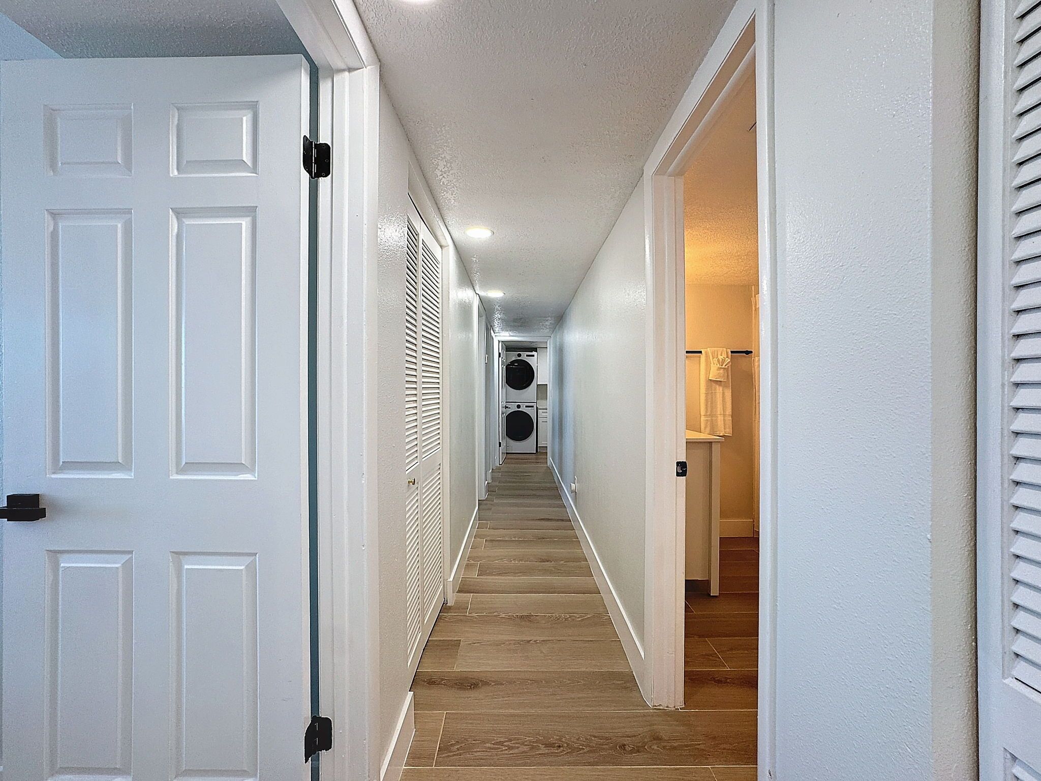 Un pasillo con piso de madera, paredes blancas y una puerta con picaporte negro.