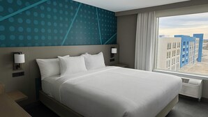 A hotel room with a large bed, two bedside lamps, a window with a view of buildings, and a wall with a blue polka dot pattern. - Comfort Inn & Suites Colby (Colby)