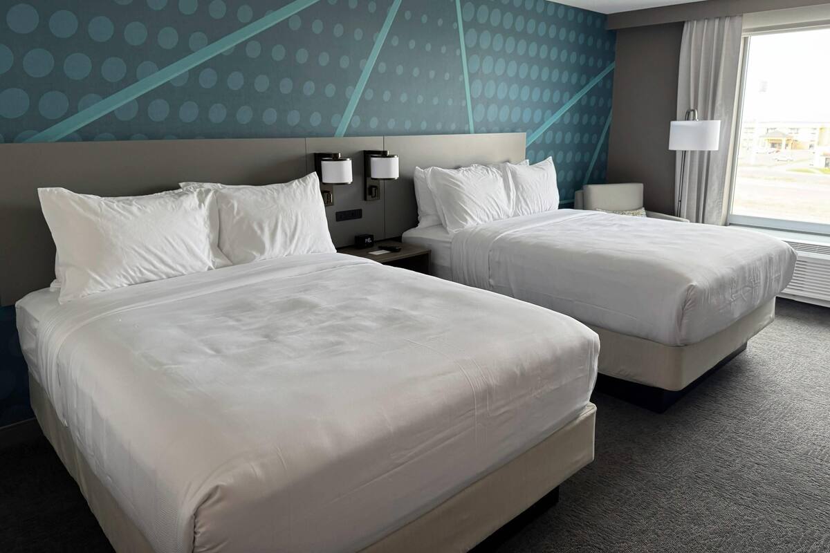 A hotel room with two beds, a large window, and a wall with a geometric pattern.