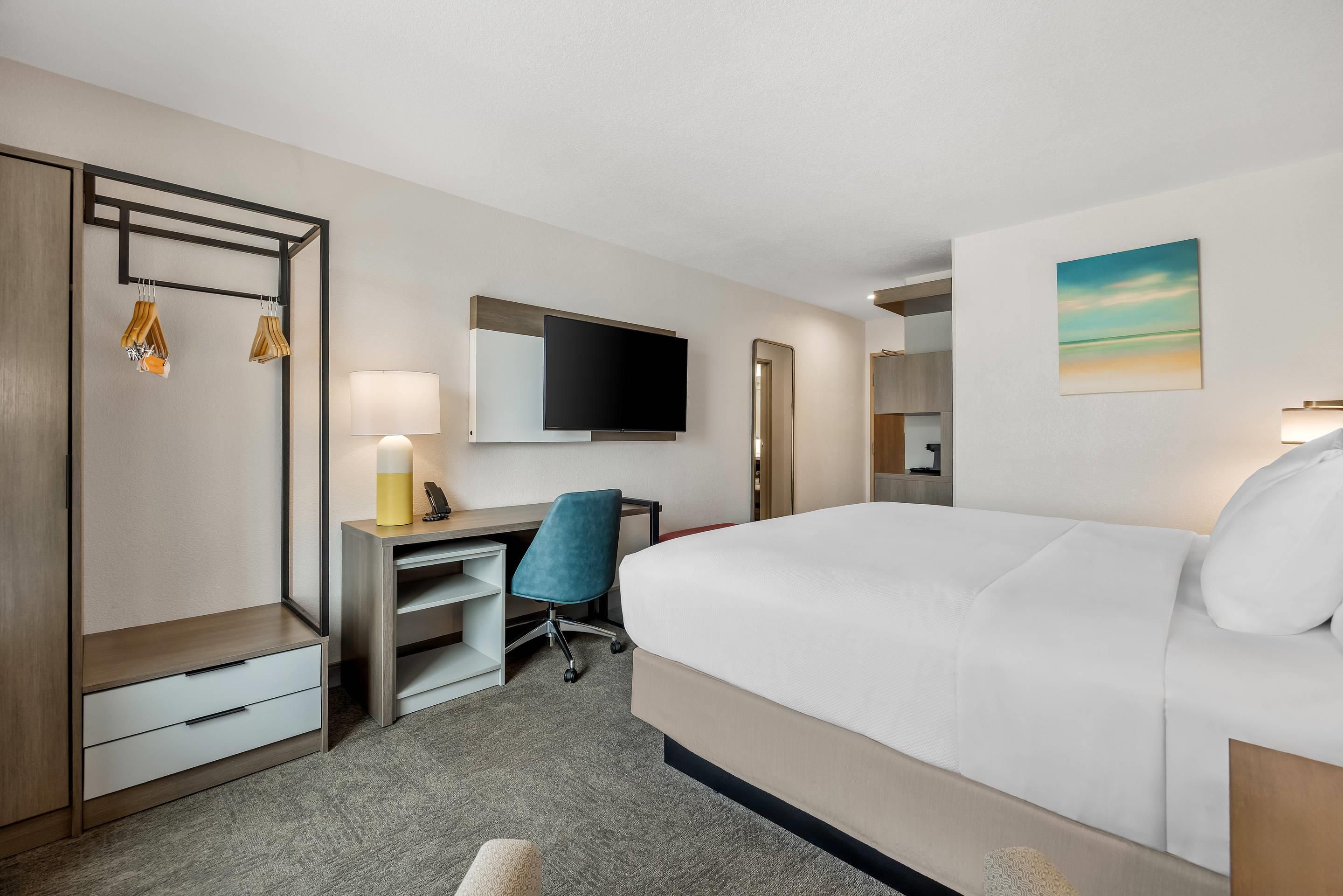 Une chambre d’hôtel avec un lit, un bureau, une chaise, une télévision et un tableau au mur.